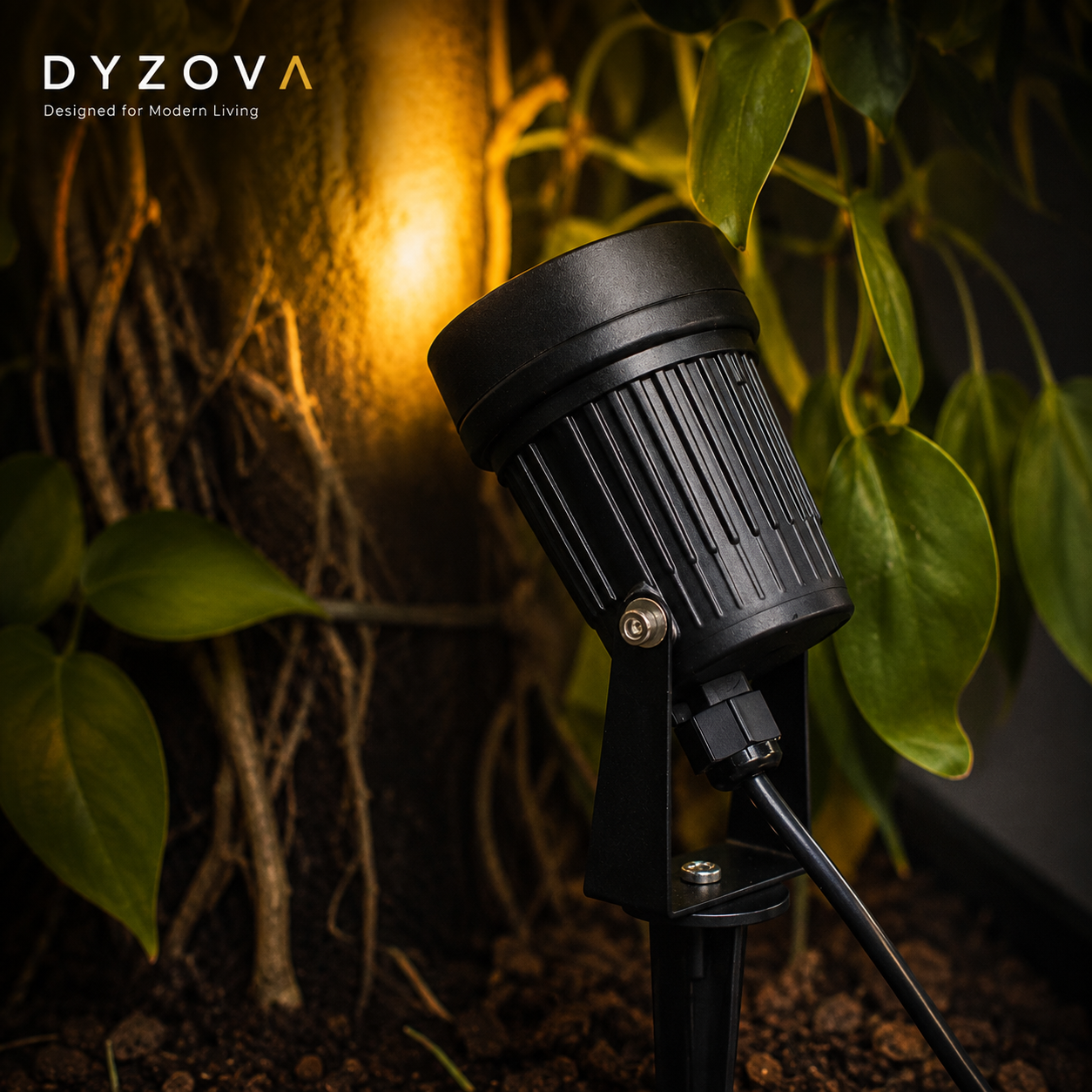 A black DYZOVA landscape garden spotlight with a ribbed cylindrical head and adjustable stake, shown lit and casting a warm yellow glow on a tree trunk, surrounded by green foliage.