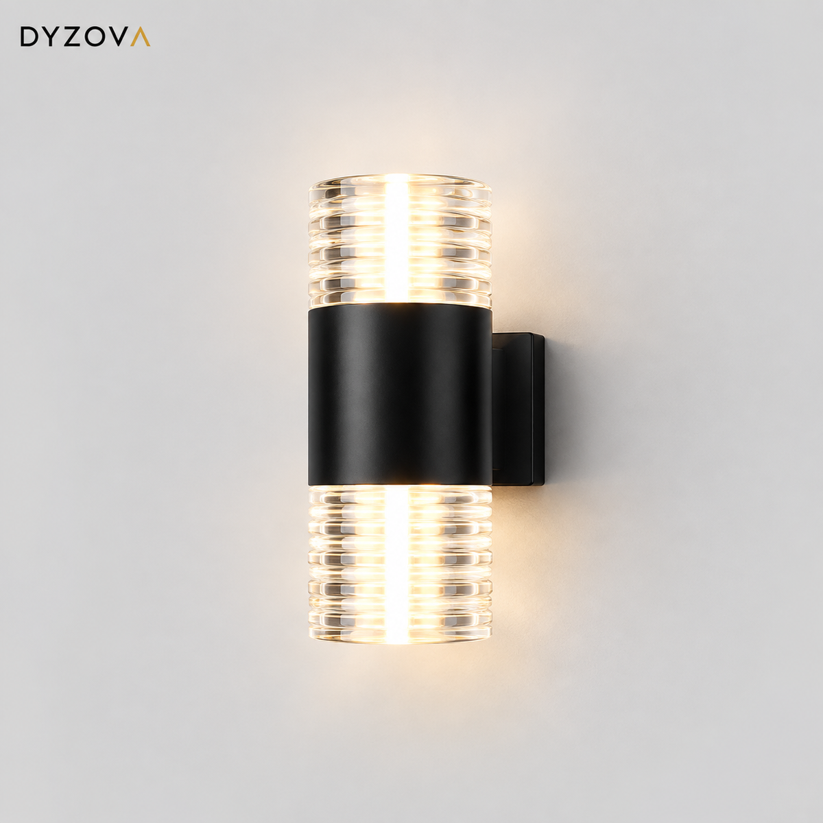 A modern wall-mounted light fixture by DYZOVA, featuring a matte black cylindrical center band and two ribbed clear glass shades glowing with warm white light, shown against a light gray wall.