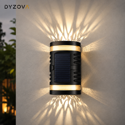 A cylindrical outdoor wall sconce by DYZOVA, featuring a black body with gold accent bands and a dark blue solar panel, mounted on a textured wall and casting warm light rays outward.