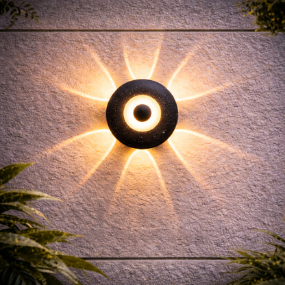 Wall-mounted outdoor light fixture on a textured wall with plants around