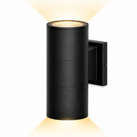 A modern black cylindrical outdoor wall light with a warm yellow glow emanating from the top and bottom, shown against a solid white background.