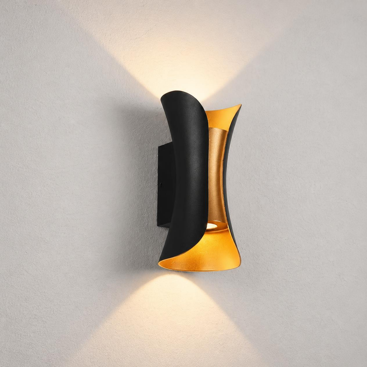 A modern wall-mounted light fixture with a curved black outer shade and a brushed gold inner accent, shown lit against a light gray textured wall.