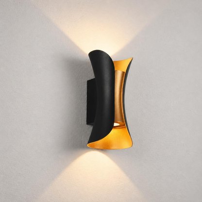 A modern wall-mounted light fixture with a curved black outer shade and a brushed gold inner accent, shown lit against a light gray textured wall.