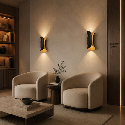Two modern beige armchairs in a warm, minimalist lounge setting with a low wooden coffee table, a side table with a vase, and two black and gold wall sconces mounted on a textured beige wall.