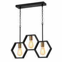 A modern three-light linear pendant chandelier with a matte black rectangular ceiling canopy, chains, and three interlocking hexagonal metal frames holding warm Edison-style bulbs.